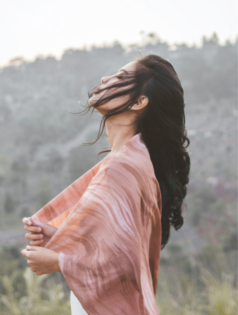 A woman standing on a mountain at sunset, arms open, symbolising clarity, freedom, and aligned business growth.